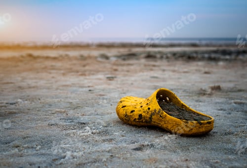 Preview: very dirty yellow Shoe on the shore of a salt lake on a Sunny day.