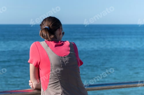 Preview: Woman dreams of traveling and looks at sea. Rear back view, copy space