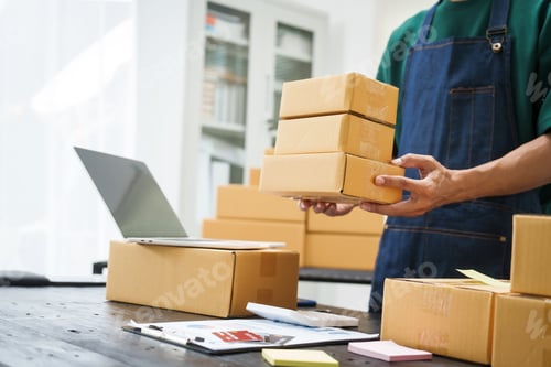 Preview: A man is working at his desk, preparing parcel boxes for shipment. He checks packs items carefully