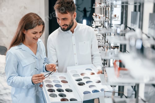 Preview: Bunch of replaceble lenses. Man and woman in the glasses store. Helping to choose product