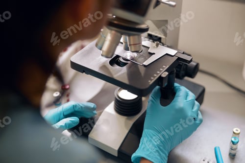 Preview: Lab assistant in latex gloves looks into microscope at sample in laboratory closeup