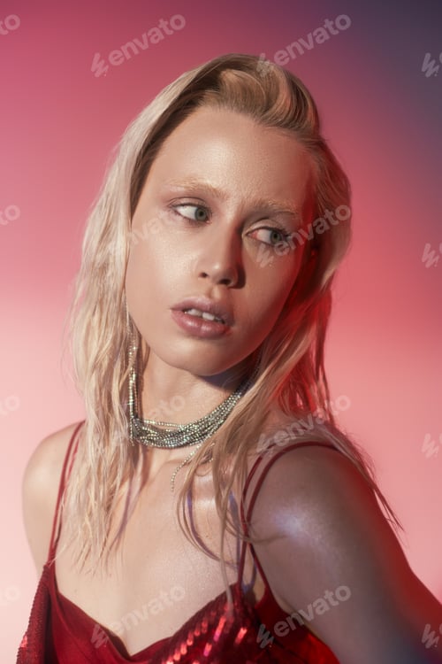 Preview: pretty blonde woman in red dress with sequins and luxury jewelry posing on pink background