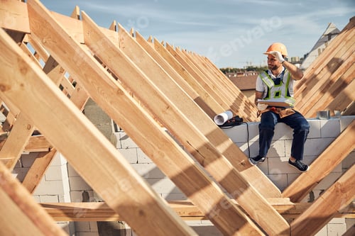 Preview: Hard-working builder sitting near a wooden roof frame
