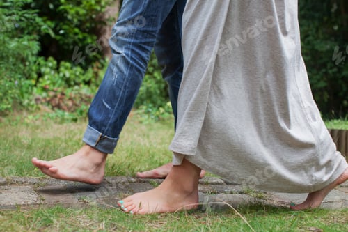 Preview: Couple wearing skinny jeans and maxi dress walking barefoot in garden