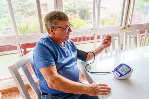 Preview: Senior man measuring blood pressure with digital monitor at home