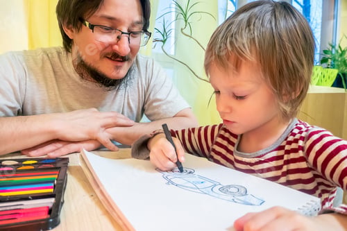 Preview: Bearded man and cute boy drawing pictures while spending time at home together.