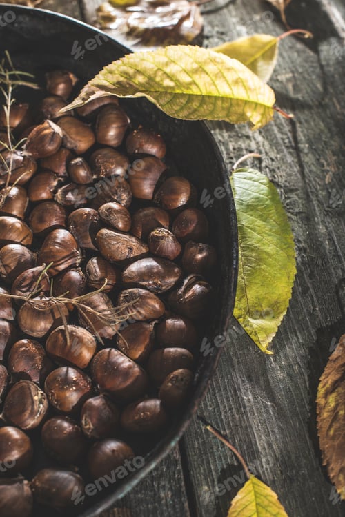 Preview: Pan of roasted sweet chestnuts and autumn leaves on wood
