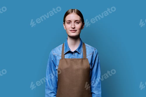 Preview: Portrait of young smiling confident woman in apron on blue background