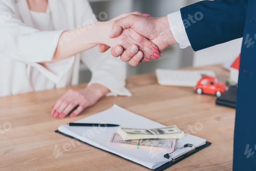 Preview: partial view of woman shaking hands with businessman near dollar banknotes on table