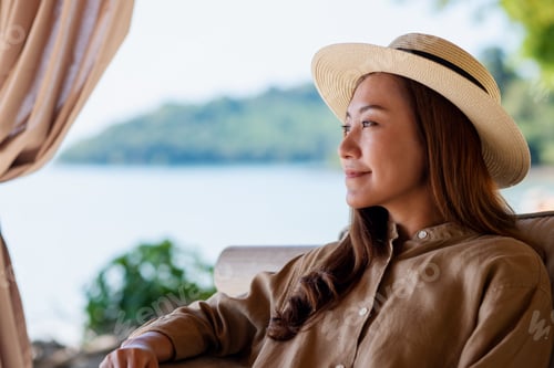 Preview: Portrait image of a beautiful young asian woman with hat sitting and looking at the beach and sea