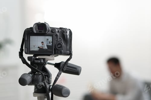 Preview: Man sitting on sofa in studio, focus on video camera recording him