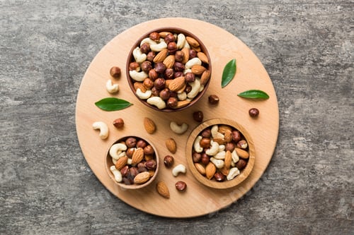 Preview: Mixed Nuts Composition with Green Leaves on Round Board