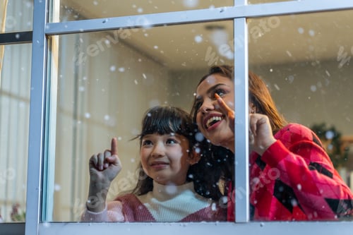 Preview: Adorable child looking at the window and admire snowflakes with mother.