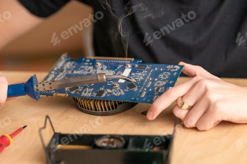 Preview: a young man solders a burnt-out microcircuit with a soldering iron