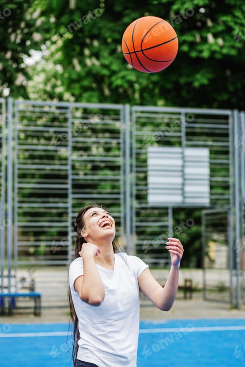 Preview: Young athletic woman is training to play basketball on modern outdoor basketball court. Happy woman