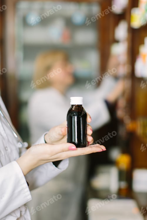 Preview: Smiling attractive young lady pharmacist holding a bottle of medicines in her hand with focus to her