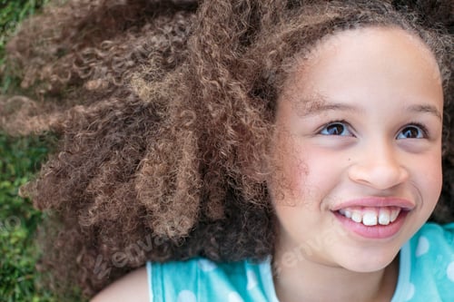 Preview: Young girl lying on grass, smiling offcamera with joy.