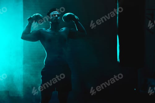 Preview: Silhouette of an unrecognizable boxer man sparring with a punching bag in a dark gym. Male athlete