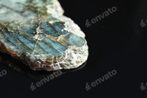 Vista previa: Beautiful labradorite gemstone on black background, closeup. Space for text