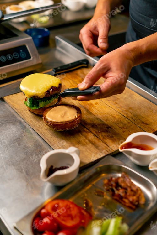 Preview: A close-up of a chef preparing a burger with beef patty with vegetables and cheese in the kitchen