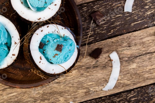 Preview: Blue ice cream with chocolate in coconut bowl on wooden background.