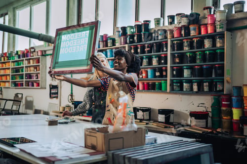 Preview: Interracial printing shop workers checking out silk screen frame.