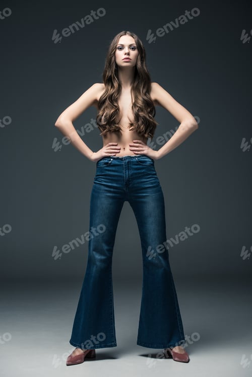 Preview: beautiful half naked girl with long hair posing in flare jeans, on grey