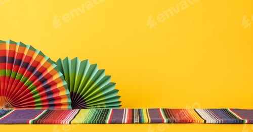 Preview: Decorative setup of multicolored Mexican fans and a serape, set on a vibrant yellow background