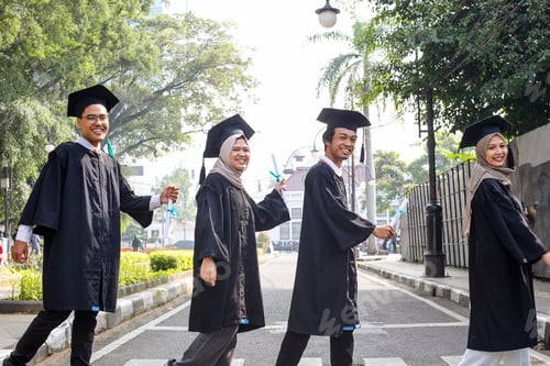 Preview: Group of happy smiling diverse student in graduation clothes cross the street and looking at camera.