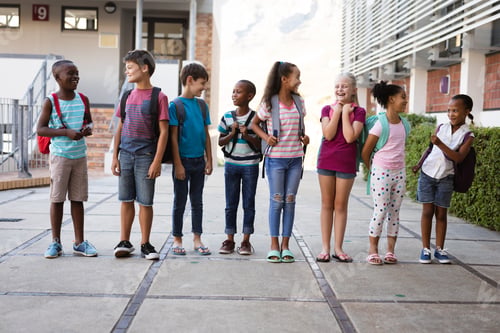 Preview: Group of diverse students with backpacks smiling while looking at each other at school
