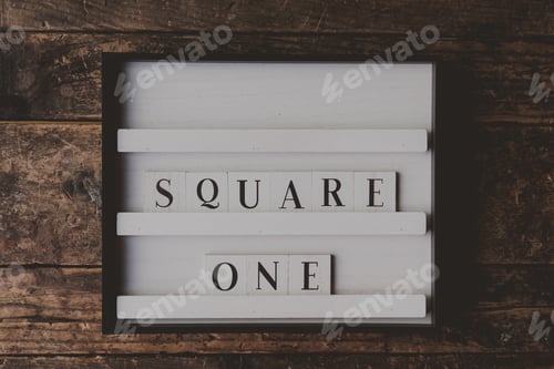 Preview: White sign with a writing "Square one" on it on a wooden brown background