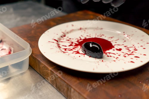 Preview: close-up in professional kitchen with a chef in black gloves laying out dessert on a plate
