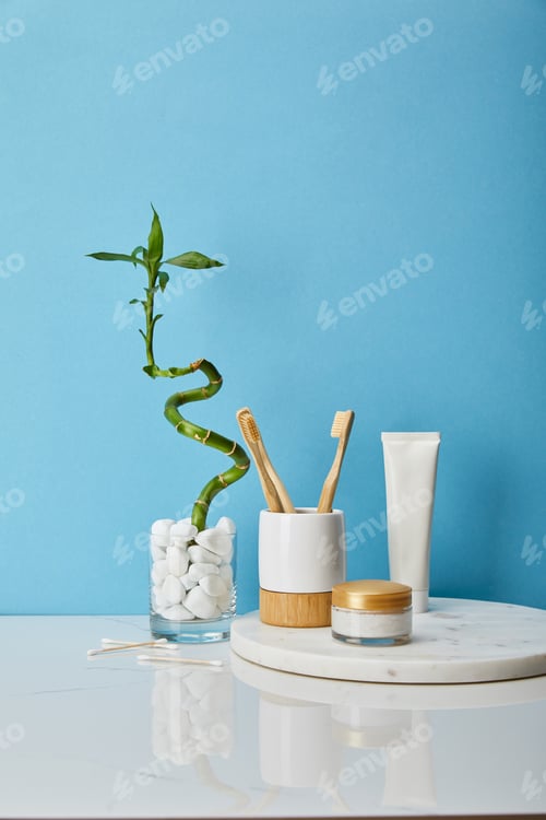 Preview: toothbrushes in holder, cosmetic cream and toothpaste in tube on round board near green bamboo stem