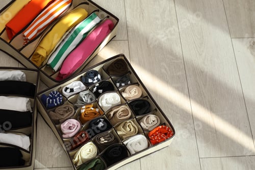 Preview: Organizers with folded clothes on wooden floor, above view. Space for text