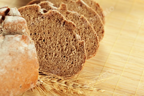 Preview: Freshly baked bread slices prepared on a wooden surface with wheat nearby