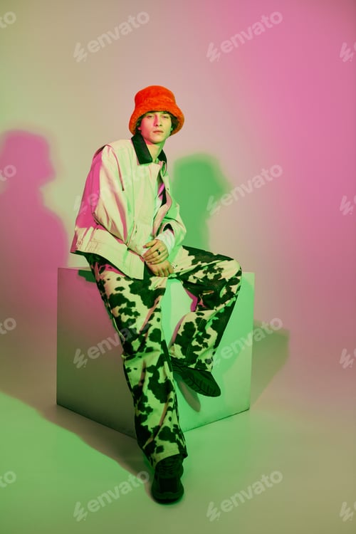 Vista previa: Stylish young man in vibrant fashion attire poses confidently against artistic background