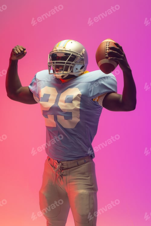 Preview: African american male american football player holding ball with neon pink lighting