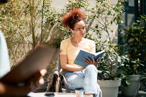 Preview: Young woman studying from a book while having coffee break at campus.