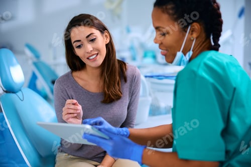 Preview: Smiling woman and her dentist using digital tablet during appointment at dental clinic.