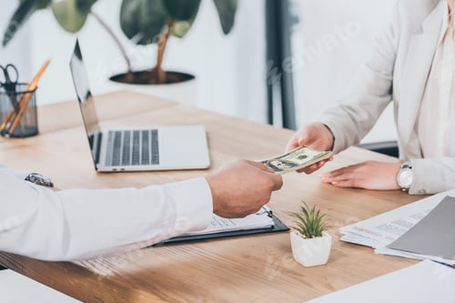 Preview: cropped view of businessman giving money to woman at workplace, compensation concept