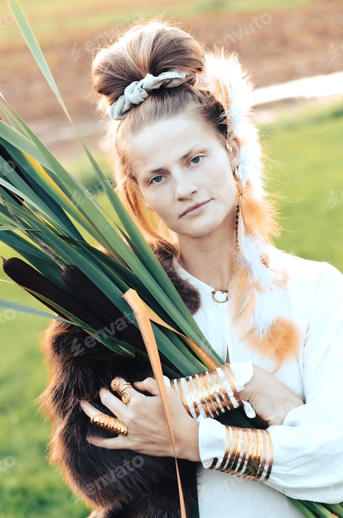 Preview: Strong young woman with a bulrush grass reed on rural field background at sunset