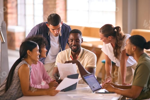 Preview: Multi-Cultural Business Team Meeting Around Desk In Modern Open Plan Office Discussing Documents