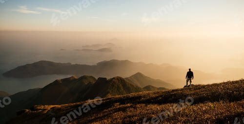 Preview: Hiker admiring the vast horizon at sunrise on a mountain trail