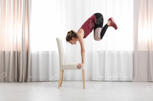 Preview: Young woman exercising with chair indoors. Home fitness