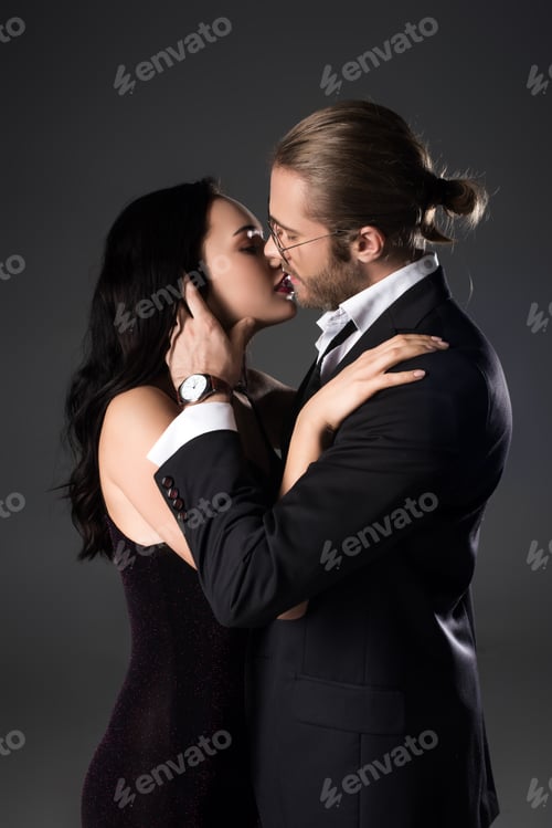 Preview: sensual couple in black suit and dress kissing isolated on grey
