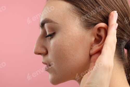 Preview: Sound. Woman showing hand to ear gesture on pink background, closeup