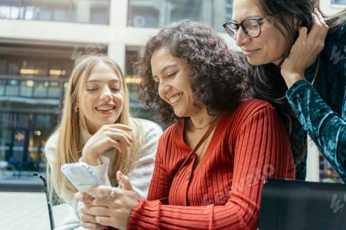 Preview: Three smiling women sharing a moment while looking at a smartphone together, Berlin, Germany