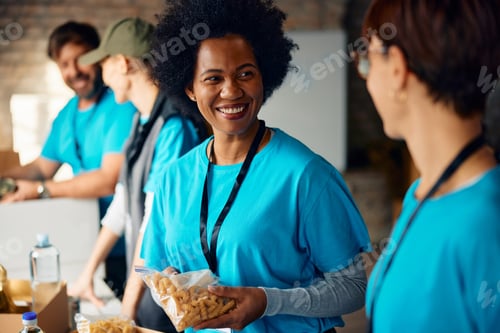 Preview: Happy black volunteer talking to her coworker while working at food bank.