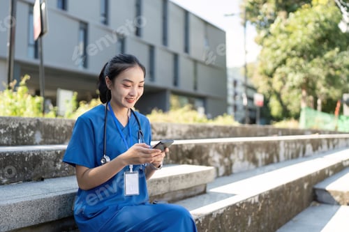 Preview: Nurse sitting on stairs, smiling while using her smartphone during a break in healthcare setting
