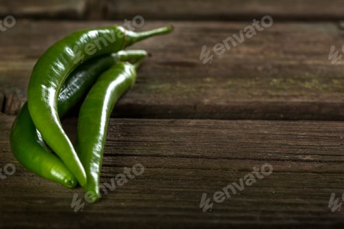 Preview: Three green hot chilli peppers over old rustic wooden table